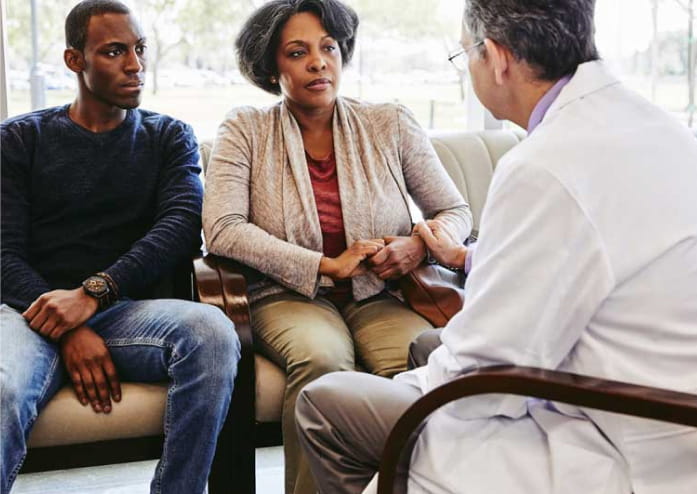 older male doctor discussing health issues with a middle aged couple on a couch in the office